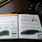 Open notebook with Diamine Green/Black ink writing samples and ink bottle on wooden desk