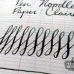 Close-up of black ink pen strokes and cursive writing on lined paper with Diamine ink review text
