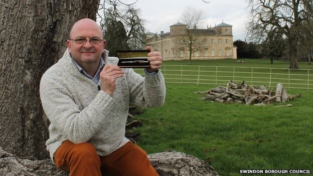 Man holding wooden pens made from 300-year-old fallen tree with historic building in background