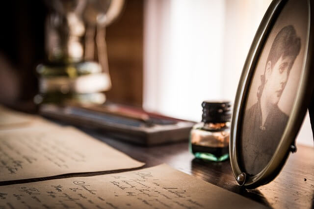Vintage handwritten letters with ink bottle and framed black and white portrait on wooden table
