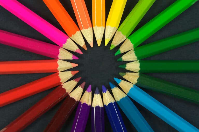 Circle of sharpened colouring pencils arranged by colour on dark background