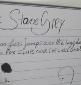 Handwritten text showing Graf Von Faber-Castell Stone Grey ink sample on lined paper with ink blot and musical note