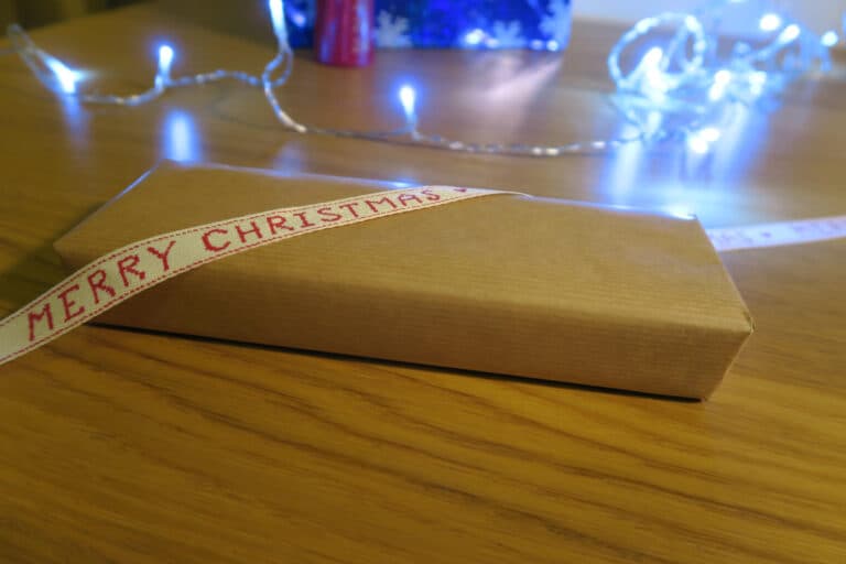 Christmas gift wrapped in brown paper with Merry Christmas ribbon on wooden table with fairy lights