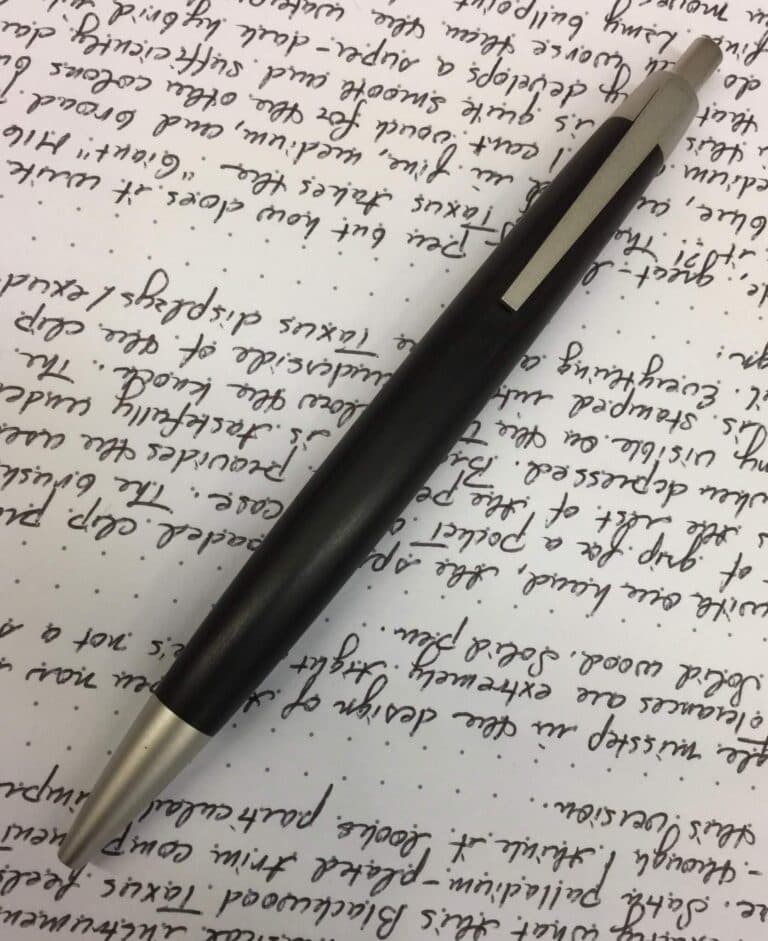 Black and silver retractable ballpoint pen on handwritten dotted paper background