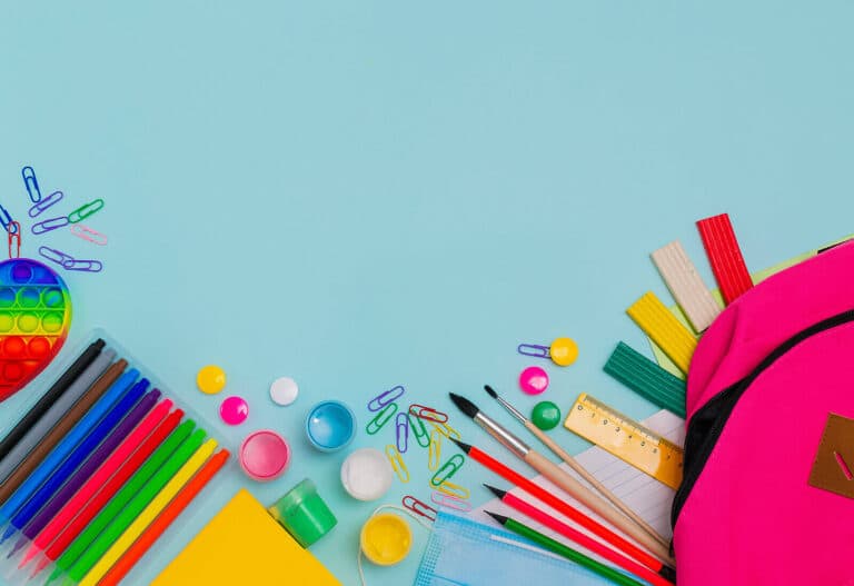 Bright colourful stationery including pens, pencils, paperclips and a pink backpack on blue background
