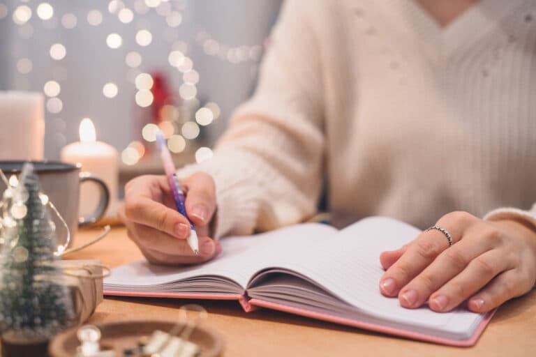 Woman hand holding pen on notepad at home on winter holidays xmas.