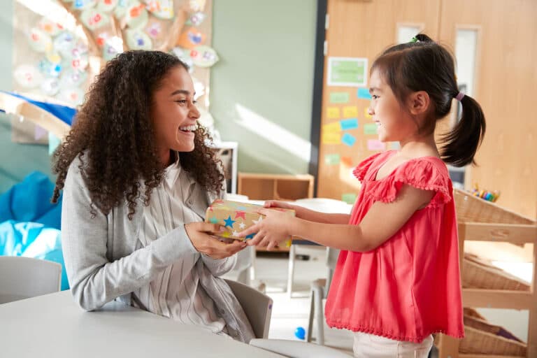 A teacher receiving a wrapped gift from a pupil in a classroom.