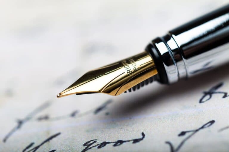 Close-up of a gold nib fountain pen writing on paper with cursive handwriting visible