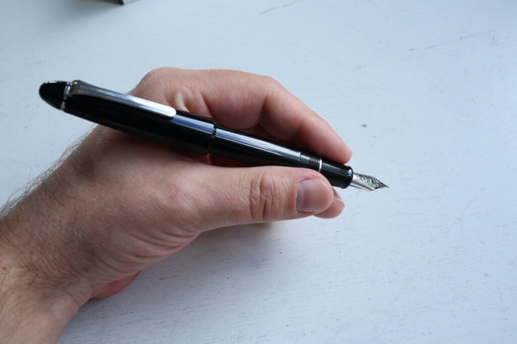 A posted Sailor 1911 Ringless fountain pen in Simply Black being held in a hand