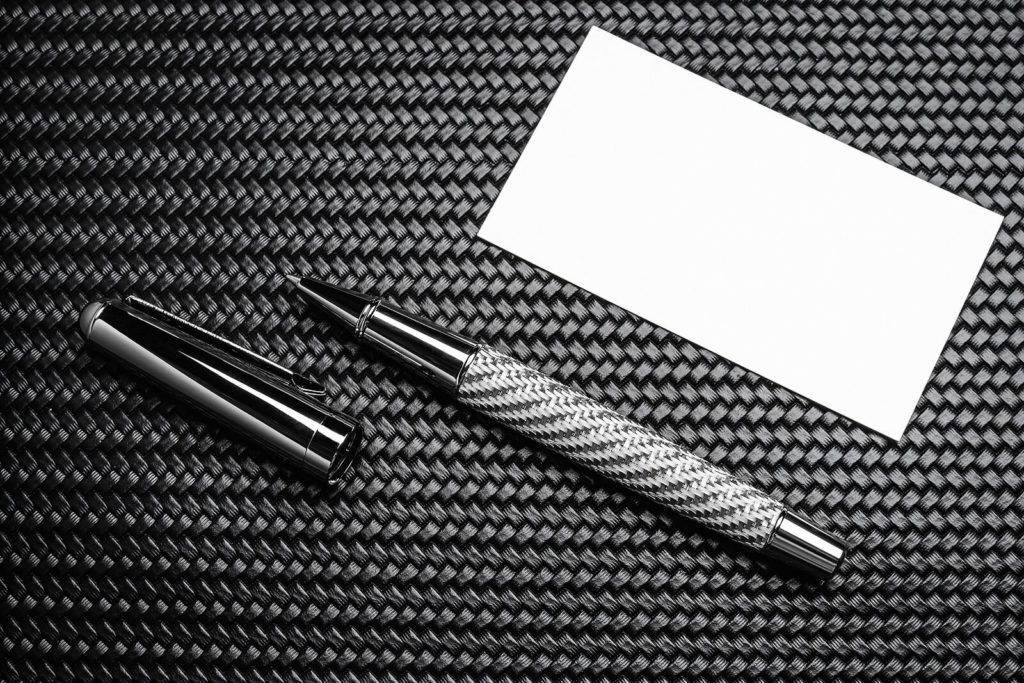 A luxury rollerball pen sat on a carbon background with a sheet of paper.