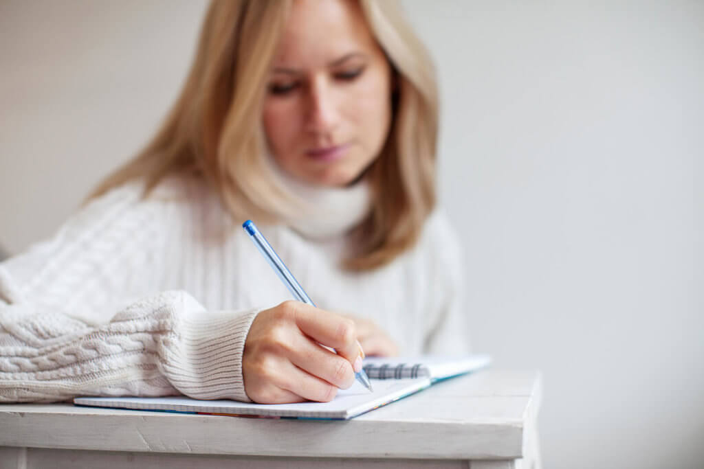 A blonde woman writing with a pen in a notebook