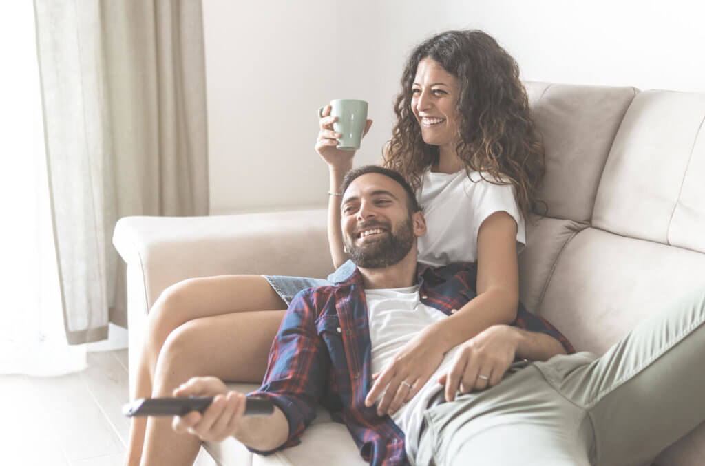 A young couple watching TV together, sat on a sofa