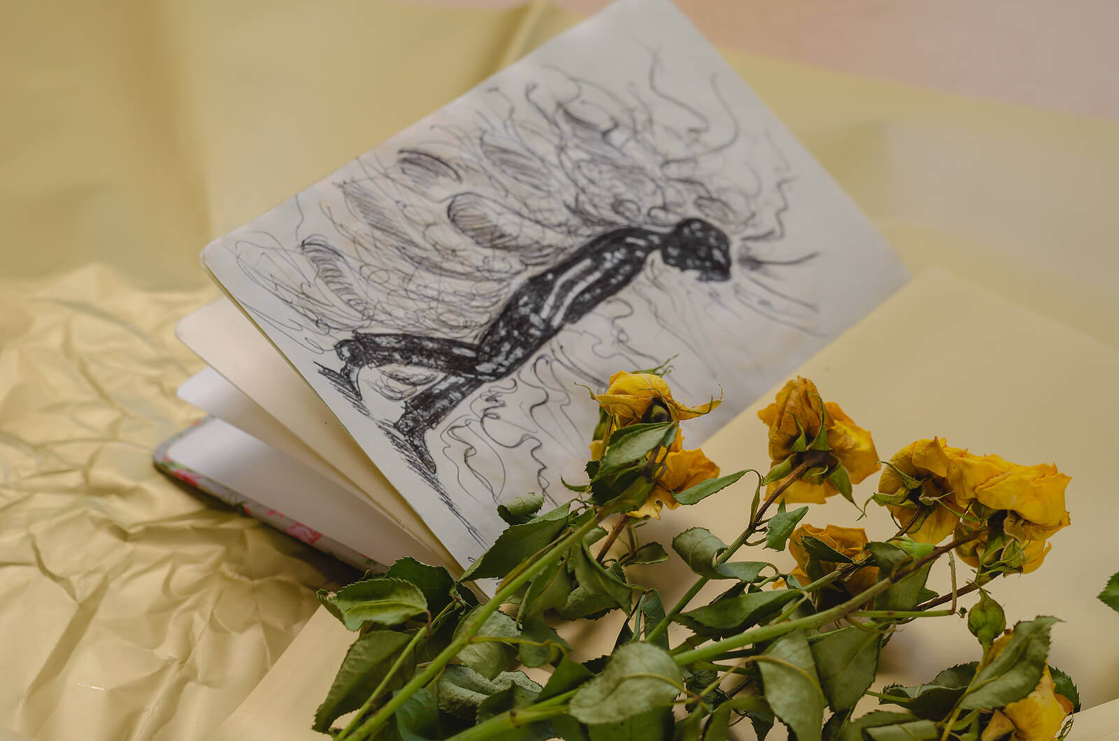 A drawing in a notebook and a fading bouquet of yellow roses.