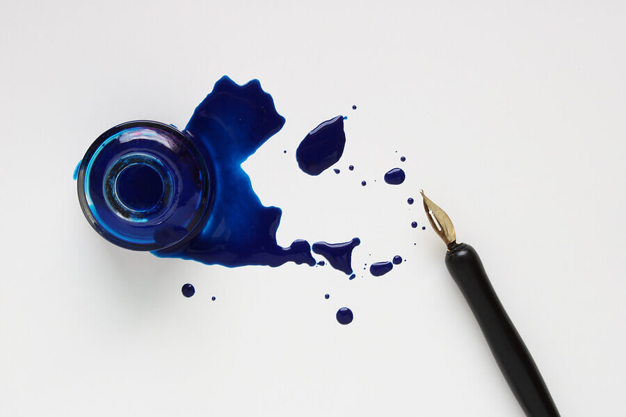 Bottle of ink with fountain pen and spilled ink.