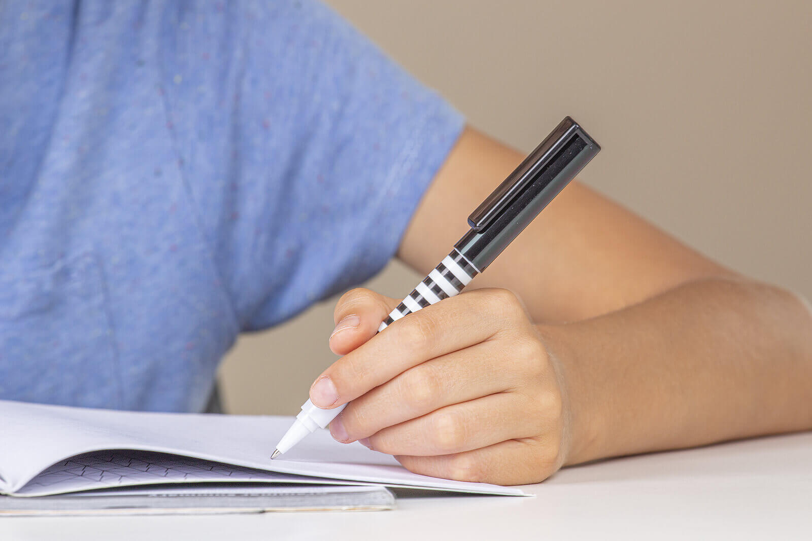 Boy hand holding pen in left hand and writing in a notebook, doing homework.