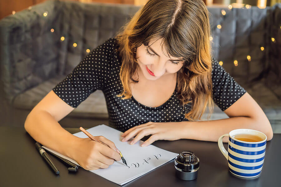 Calligrapher Young Woman writes phrase on white paper. Inscribing ornamental decorated letters.
