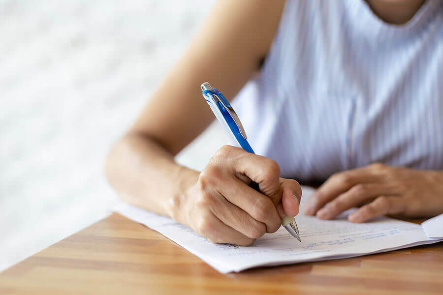 Close up hand of business women use pen writing document paper. Female hand close up writing with a blue pen on a white sheet.