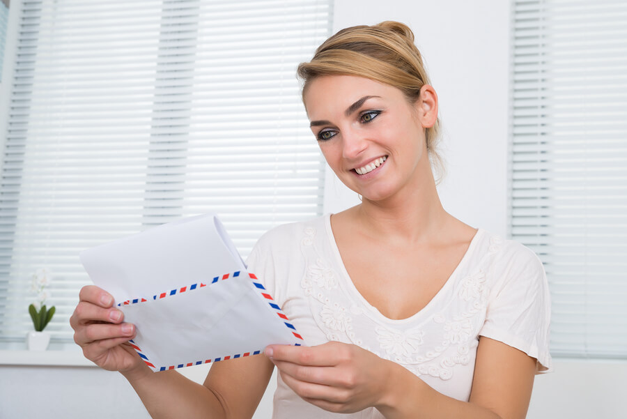 Happy young woman reading letter while sitting at home