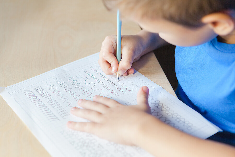 Kid doing lesson at home. Child boy writing in worksheet with pencil.