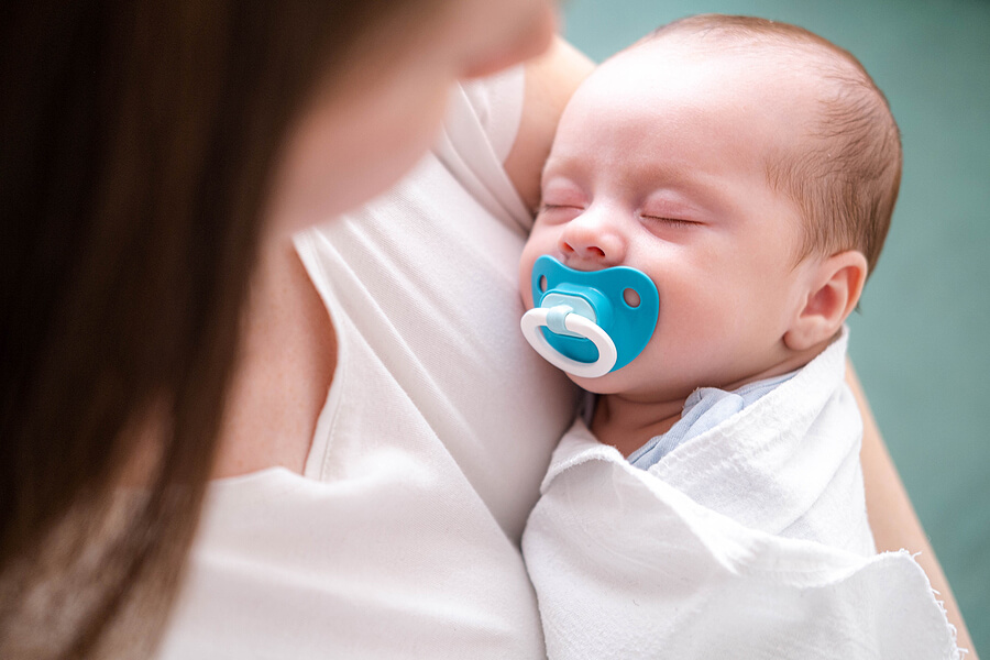 Little newborn baby boy sleeping with baby dummy on mother hands at home, Mom puts baby to sleep during the day.