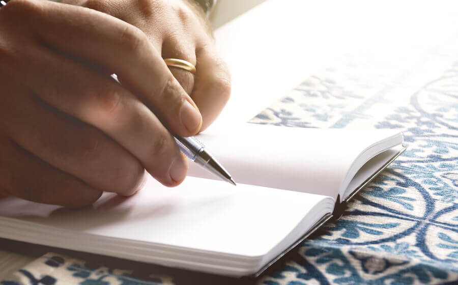 a man's hand writing in a book with a pen