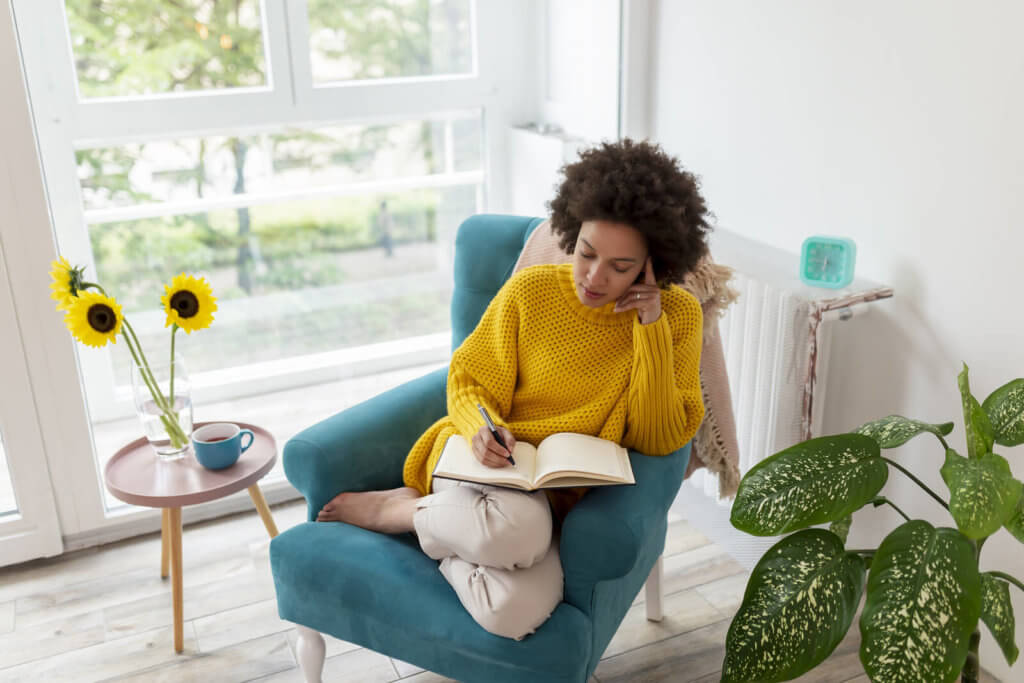 a woman writing in a book while sat down in a blue chair