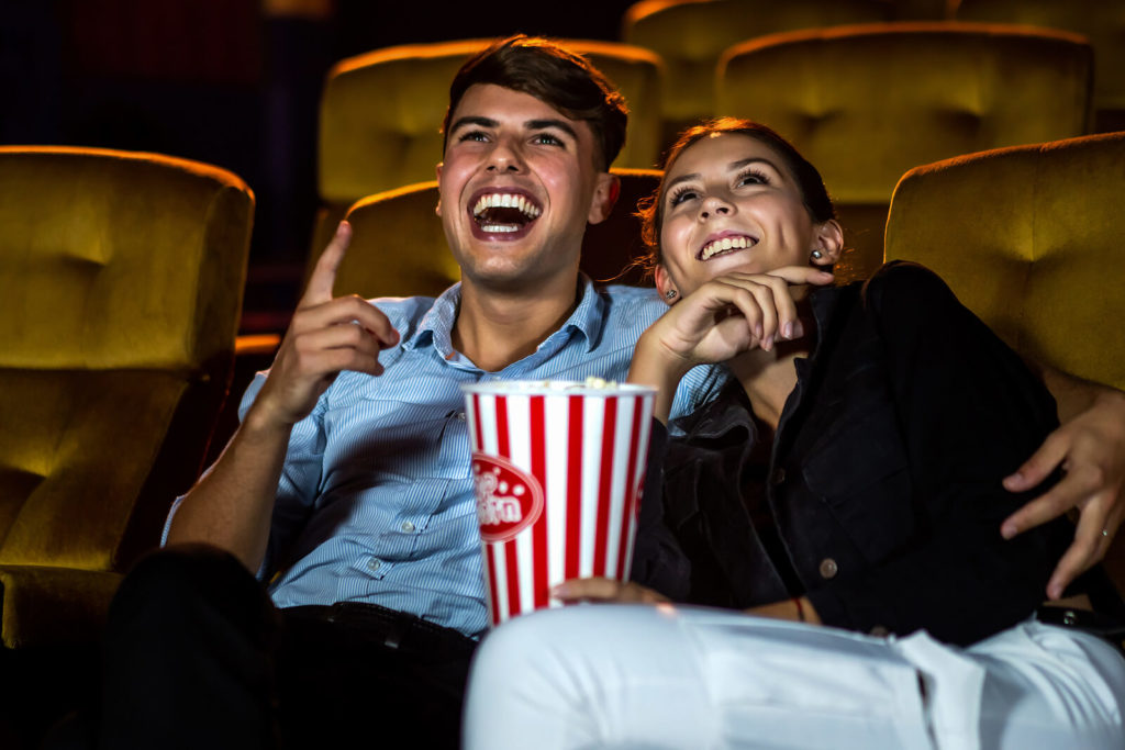 An audience of two people watching a film/movie at the cinema, while eating popcorn.