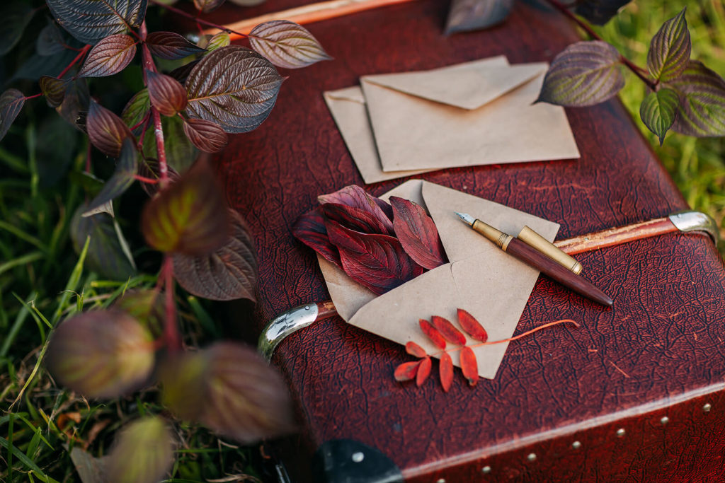 A fountain pen and envelopes placed on a vintage suitcase in autumn.
