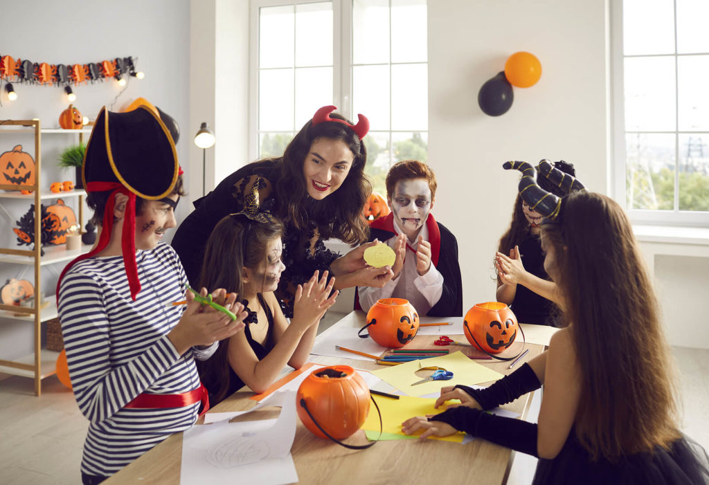 A Halloween classroom where the teacher and pupils are all in costumes and crafting at a table.
