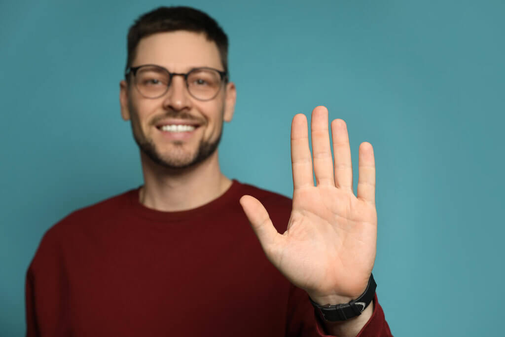 A man in a red jumper stood against a blue background, holding his left hand up and forwards toward the camera, representing left-handedness