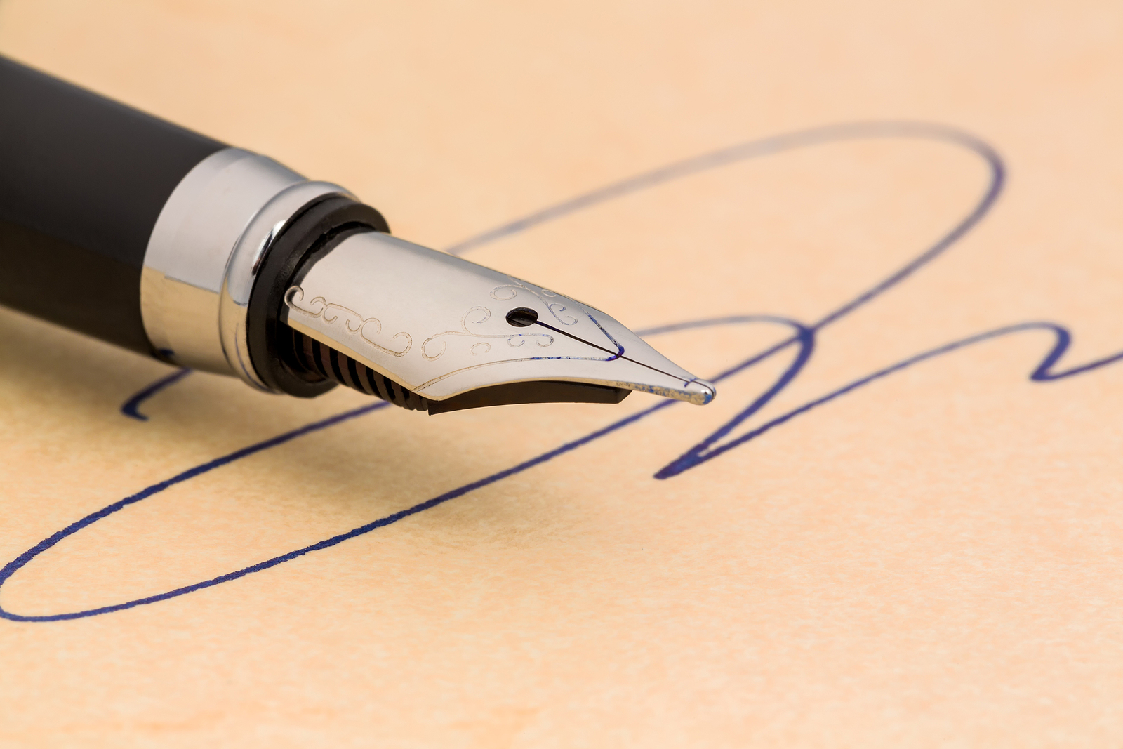 alt="" Close-up image of the silver nib of a black fountain pen. The pen is on an unlined page of parchment where a signature has been written with blue ink.