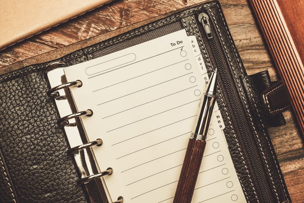 A rollerball pen sat on a personal organiser which is open on a to-do list page.