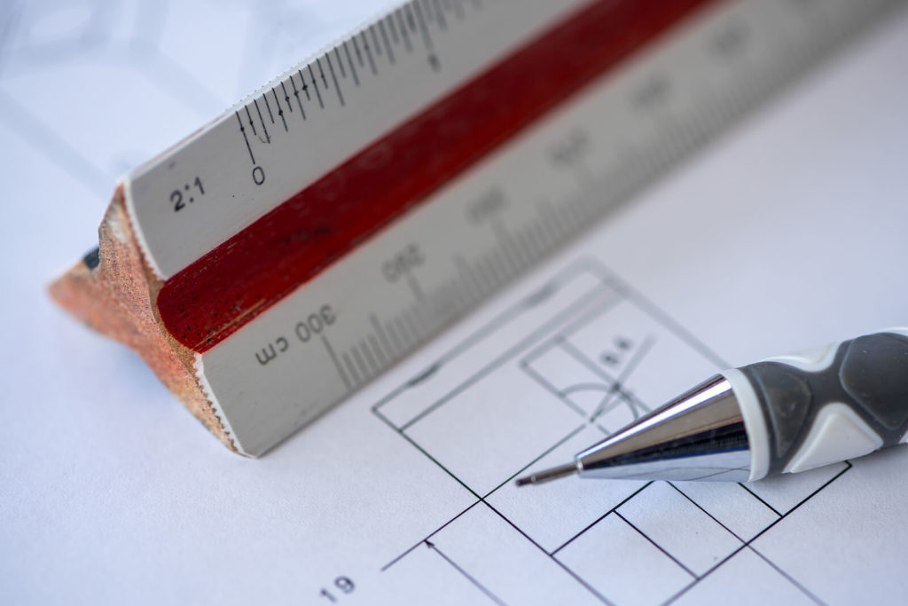 Close-up of a mechanical pencil and a wooden ruler sat on an architect's blueprint drawing.