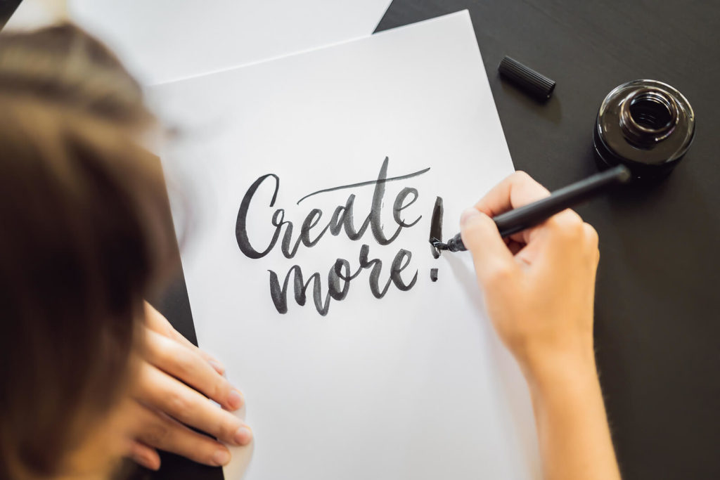 Someone creating calligraphy on paper, they've written "Create more"