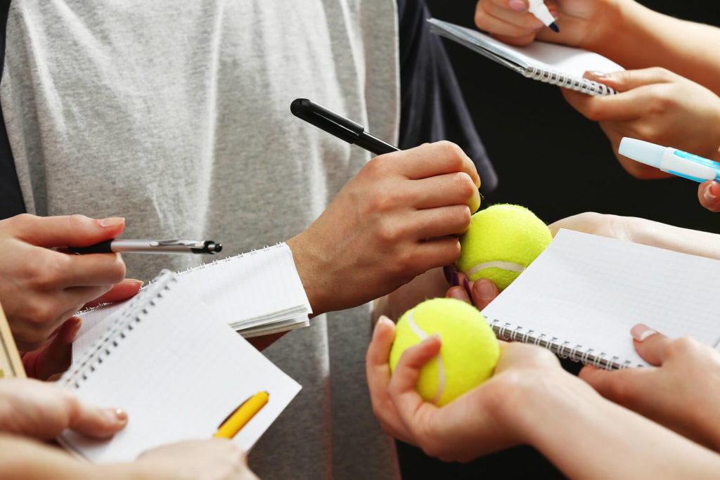 A sportsman signing tennis balls and notebooks