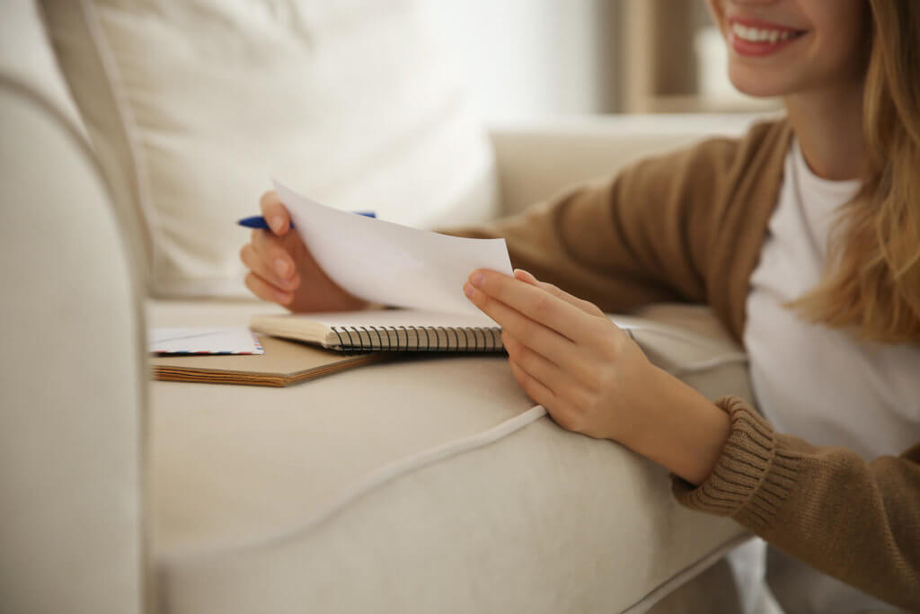 A woman writing a letter on her sofa and smiling