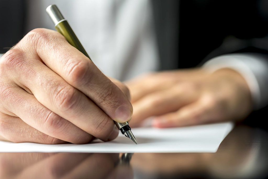 A man holding a fountain pen and writing on paper.