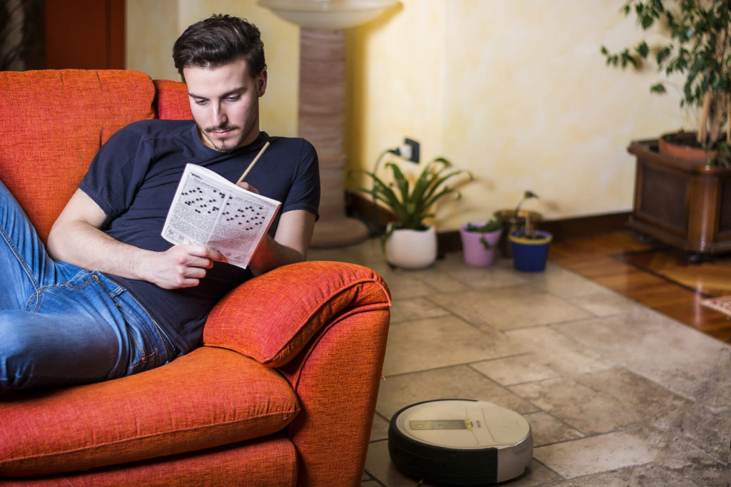 A young man sat on a red sofa completing a crossword.