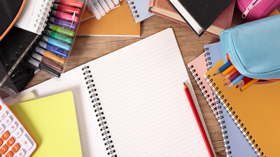 Busy student's desk with open notebook school bag text books and various pencils and crayons.