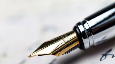 Close-up of a gold nib fountain pen writing on paper with cursive handwriting visible